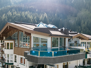 Außenansicht des Hotels Neuhintertux mit Skypool und Blick auf den angrenzenden Wald in den Tiroler Alpen.